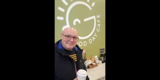 Smiling man holding coffee cup in front of Good Day Cafe sign